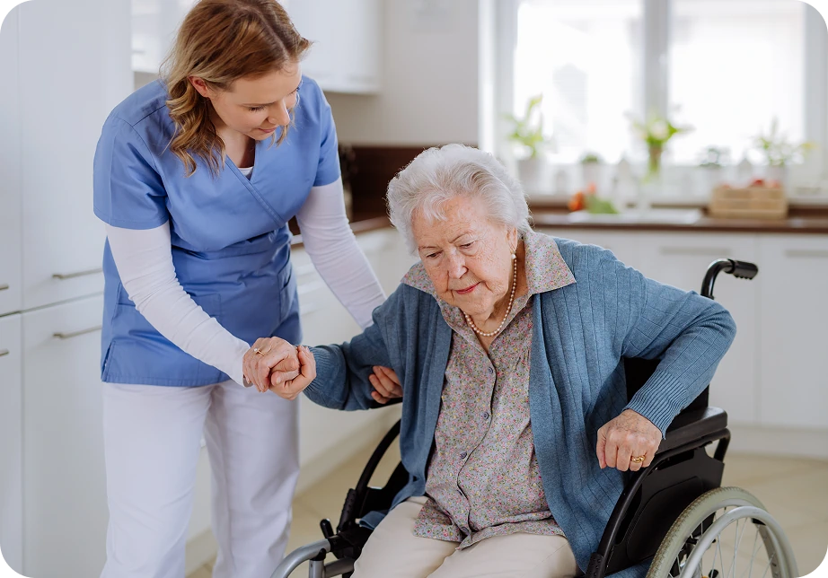 Kobieta pomagająca wstać starszej pani z wózka inwalidzkiego w kuchni